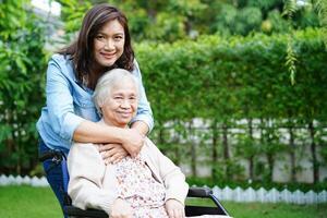 pflegekraft hilft asiatischen älteren frauen mit behinderungspatienten, die im park im rollstuhl sitzen, medizinisches konzept. foto