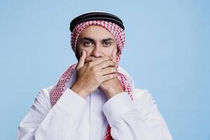 Mann tragen traditionell islamisch Kleider Abdeckung Mund mit Hände, zeigen sprechen Nein böse Zeichen Studio Porträt. Muslim Person behalten Geheimnis, präsentieren drei weise Affen Konzept foto
