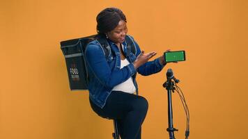 afrikanisch amerikanisch Kurier packend Zelle Telefon zeigen Grün Bildschirm Anzeige während Reiten Fahrrad. schwarz Frau demonstriert innovativ, auf dem neuesten Stand Lieferung App auf Handy, Mobiltelefon Gerät mit isoliert Attrappe, Lehrmodell, Simulation Vorlage. foto