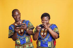 heiter afrikanisch amerikanisch Ehefrau und Mann Paar genießen Handy, Mobiltelefon Spiel Wettbewerb. lächelnd Paar spielen unterhaltsam Spiel auf Smartphones, Teilen Spaß Freizeit Aktivität zusammen foto