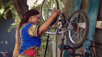 Seitenansicht Porträt von sportlich gesund schwarz Frau reparieren Fahrrad mit Fachmann Werkzeuge im Zuhause Hof. weiblich afrikanisch amerikanisch Radfahrer beurteilen und Wiederherstellen beschädigt Fahrrad außen. foto