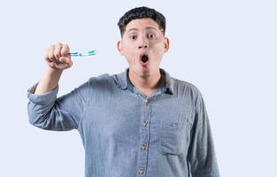 überrascht jung Mann halten Zahnbürste mit Zahnpasta isoliert. erstaunt Person halten Zahnbürste suchen beim Kamera foto