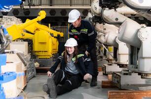 ein weiblich Arbeiter litt ein Bein Unfall während Arbeiten im Roboter Waffen Fabrik und männlich Techniker ist Portion und Bereitstellung zuerst Hilfe. foto