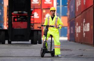 Porträt von ein Warenhaus Arbeiter Sprechen auf ein Walkie Talkie mit ein Mitarbeiter im ein leeren Container Warenhaus während Fahren ein Roller zu prüfen Arbeit foto