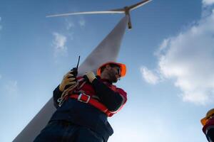 niedrig Winkel Aussicht von ein männlich Ingenieur Stehen im Vorderseite von ein Wind Turbine, mit das Walkie Talkie zu kommunizieren mit Mitarbeiter foto