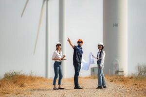 zurück Aussicht von Gruppe Ingenieure Gehen und suchen beim Wind Turbinen im ein Windmühle Bauernhof. foto