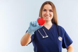 weiblich Arzt mit Stethoskop halten rot Herz auf Blau Hintergrund foto