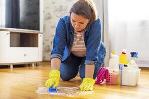 ein jung Frau im schützend Handschuhe wäscht das Fußboden mit ein Bürste und Waschmittel foto