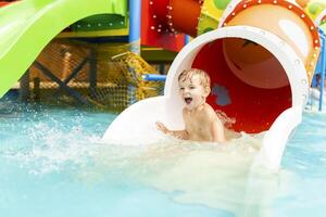 wenig Junge spielen auf Wasser rutschen im draussen Schwimmbad auf ein heiß Sommer- Tag foto