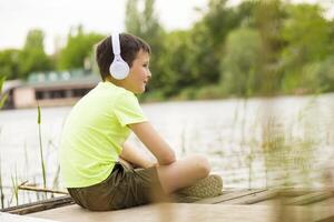 ein Junge mit Kopfhörer Hören zu Musik- beim Seeufer foto