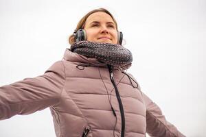 froh jung Frau im Jacke Hören zu Musik, entspannend im ein Park foto