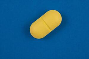 Oval geformt Gelb Pille im Makro Aussicht isoliert auf Blau Hintergrund foto
