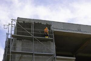 Arbeiter Verputzen das draußen von ein Gebäude auf Gerüst. Arbeit Sicherheit Konzept foto