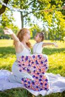 heiter Mutter und Tochter haben Spaß auf Kind Geburtstag auf Decke mit Papier Dekorationen im das Park foto