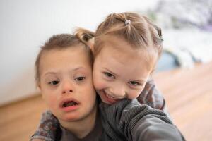 klein Junge mit Nieder Syndrom Theaterstücke mit seine jünger Schwester im Zuhause Schlafzimmer. hoch Qualität Foto