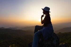 Person auf oben von Berg, Silhouette von jung Frau Sitzung auf ein Felsen suchen zu das Horizont. foto
