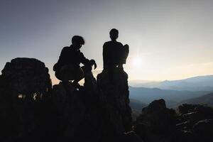 Person auf oben von Berg, Silhouette von jung Menschen Sitzung auf ein Felsen suchen zu das Horizont. foto