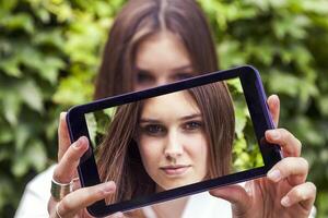 jung tausendjährig Frau nehmen ein Selfie mit Clever Telefon draußen foto