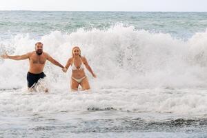 ein verheiratet Paar schwimmt im das Meer auf das Wellen, halten Hände. das Konzept von ein romantisch Ausflug foto