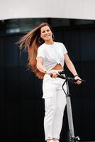 schön Mädchen im Weiß stilvoll Kleider auf ein elektrisch Roller im das Stadt foto