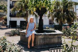 ein blond Frau im ein Sommerkleid sitzt auf das Straße von das alt Stadt, Dorf von icod de los Vinos auf das Insel von teneriffa.spanien, Kanarienvogel Inseln. foto