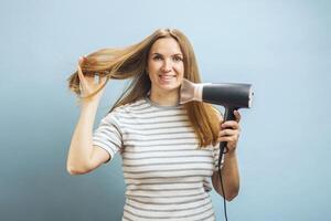Frau trocknet ihr schön lange Haar mit ein Haar Trockner gegen ein Blau Hintergrund foto