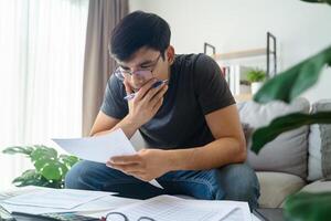 nachdenklich Mann halten Papier Arbeit Unterlagen und Stift berühren Kinn mit nachdenklich Ausdruck. foto