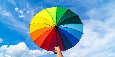 Hand halten bunt Regenbogen Regenschirm und Blau Himmel Hintergrund. LGBT, Stolz Monat, Diversität, Sonnenschutz Konzept. foto