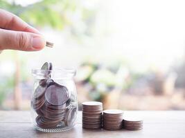 schließen oben Hand Putten Münze in Glas Flasche und Stapel von Münzen. das Konzept von Speichern Geld, finanziell, Investition und Geschäft wachsend. foto