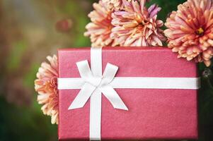 rot Geschenk Box mit Weiß Bogen und Blumen auf Grün Hintergrund mit Bokeh foto