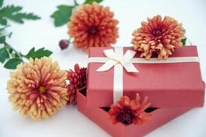 rot Geschenk Box mit Orange Chrysanthemen auf Weiß Hintergrund foto