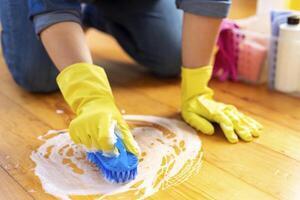 ein jung Frau im schützend Handschuhe wäscht das Fußboden mit ein Bürste und Waschmittel foto