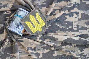 ukrainisch Heer Symbol und Bündel von Dollar Rechnungen auf Militär- Uniform. Zahlungen zu Soldaten von das ukrainisch Heer von vereinigt Zustände, Gehälter zu das Militär. Krieg Unterstützung foto