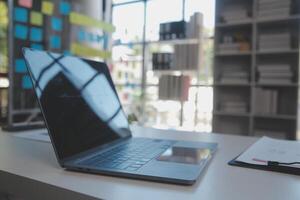 schließen oben Aussicht von einfach Arbeitsplatz mit Laptop, Notizbücher, Kaffee Tasse und Baum Topf auf Weiß Tabelle mit verschwommen Büro Zimmer Hintergrund foto