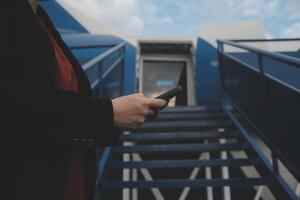 jung asiatisch Frau im International Flughafen, mit Handy, Mobiltelefon Smartphone und Überprüfung Flug beim das Flug Information Tafel foto