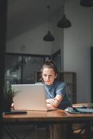 ein Frau, tief vertieft im ihr arbeiten, lehnt sich nach vorne gegenüber ihr Laptop Bildschirm, ihr Ausdruck einer von heftig Fokus und Entschlossenheit im ein gut beleuchtet modern Büro. foto