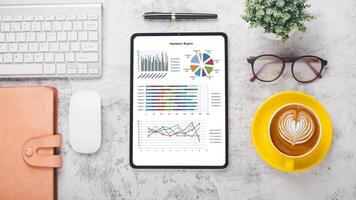 modern Büro Schreibtisch Arbeitsplatz mit Geschäft Diagramm auf Bildschirm Tablette Anzeige, Klaviatur, Maus, Notizbuch, Stift, Brille und Tasse von Kaffee, oben Aussicht eben legen mit Kopieren Raum. foto