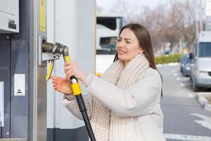 jung Frau halten ein Treibstoff Düse im ihr Hand während Auftanken Auto beim Gas Bahnhof. ein halt zum Auftanken beim das Gas Bahnhof. Betanken das Auto mit Gas. foto