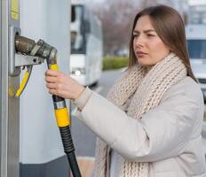 jung Frau halten ein Treibstoff Düse im ihr Hand während Auftanken Auto beim Gas Bahnhof. ein halt zum Auftanken beim das Gas Bahnhof. Betanken das Auto mit Gas. foto