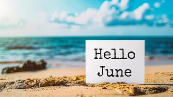 ai generiert Hallo Juni Botschaft auf Weiß Papier auf sandig Strand mit Meer und Himmel Hintergrund foto