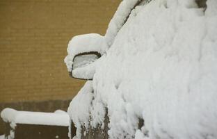 Fragment des Autos unter einer Schneeschicht nach einem starken Schneefall. Die Karosserie des Autos ist mit weißem Schnee bedeckt foto