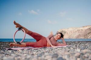 Frau Meer Pilates. sportlich glücklich Mitte alt Frau üben Fitness auf Strand in der Nähe von Meer, lächelnd aktiv weiblich Ausbildung mit Ring auf Yoga Matte außen, genießen gesund Lebensstil, Harmonie und Meditation foto