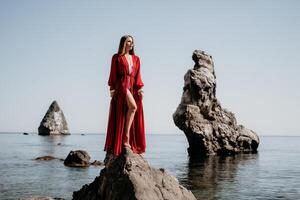 Frau Reise Meer. jung glücklich Frau im ein lange rot Kleid posieren auf ein Strand in der Nähe von das Meer auf Hintergrund von vulkanisch Felsen, mögen im Island, Teilen Reise Abenteuer Reise foto