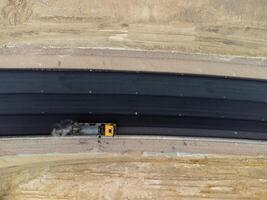 Gelb LKW Gießen Bitumen Über ein Neu Straße. Antenne Drohne Schuss. Straße Konstruktion im Fortschritt auf Steigung Natur Schlucht. Infrastruktur Entwicklung und Logistik. foto