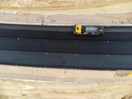 Gelb LKW Gießen Bitumen Über ein Neu Straße. Antenne Drohne Schuss. Straße Konstruktion im Fortschritt auf Steigung Natur Schlucht. Infrastruktur Entwicklung und Logistik. foto