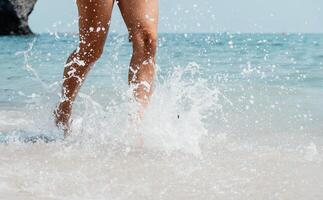 Meer Strand Reise - - Frau Gehen auf Sand Strand Verlassen Fußabdrücke im das Weiß Sand. weiblich Beine Gehen entlang das Strand barfuß, Nahansicht von das Braun gebrannt Beine von ein Mädchen Kommen aus von das Wasser. foto