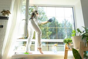 Frau manuell wäscht das Fenster von das Haus mit ein Lappen mit sprühen Reiniger und Mopp Innerhalb das Innere mit Weiß Vorhänge. Wiederherstellen bestellen und Sauberkeit im das Frühling, Reinigung warten foto