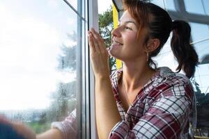 Frau manuell wäscht das Fenster von das Haus mit ein Lappen mit sprühen Reiniger und Mopp Innerhalb das Innere mit Weiß Vorhänge. Wiederherstellen bestellen und Sauberkeit im das Frühling, Reinigung warten foto