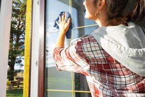 Frau manuell wäscht das Fenster von das Haus mit ein Lappen mit sprühen Reiniger und Mopp Innerhalb das Innere mit Weiß Vorhänge. Wiederherstellen bestellen und Sauberkeit im das Frühling, Reinigung warten foto