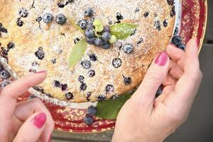 ein Frau Hand dekoriert ein frisch Kuchen mit Blaubeeren, ruckeln beim Zuhause, Essen foto